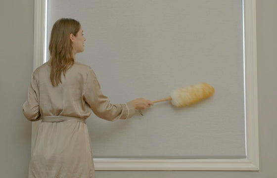 Woman is cleaning the roller shade through wool duster.