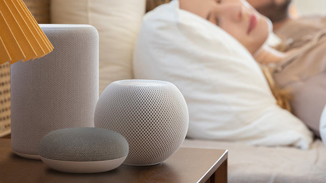 A woman is sleeping in bed, with many smart speakers on the bedside table next to her.