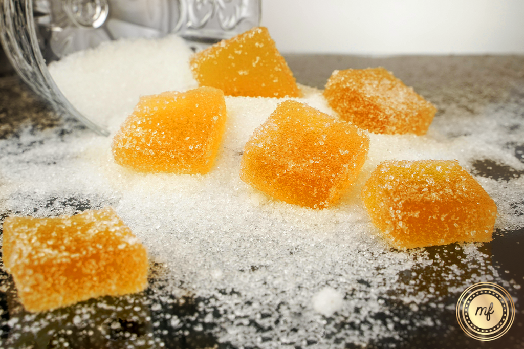 Yellow resin gummies fall onto a black surface with sugar scattered around