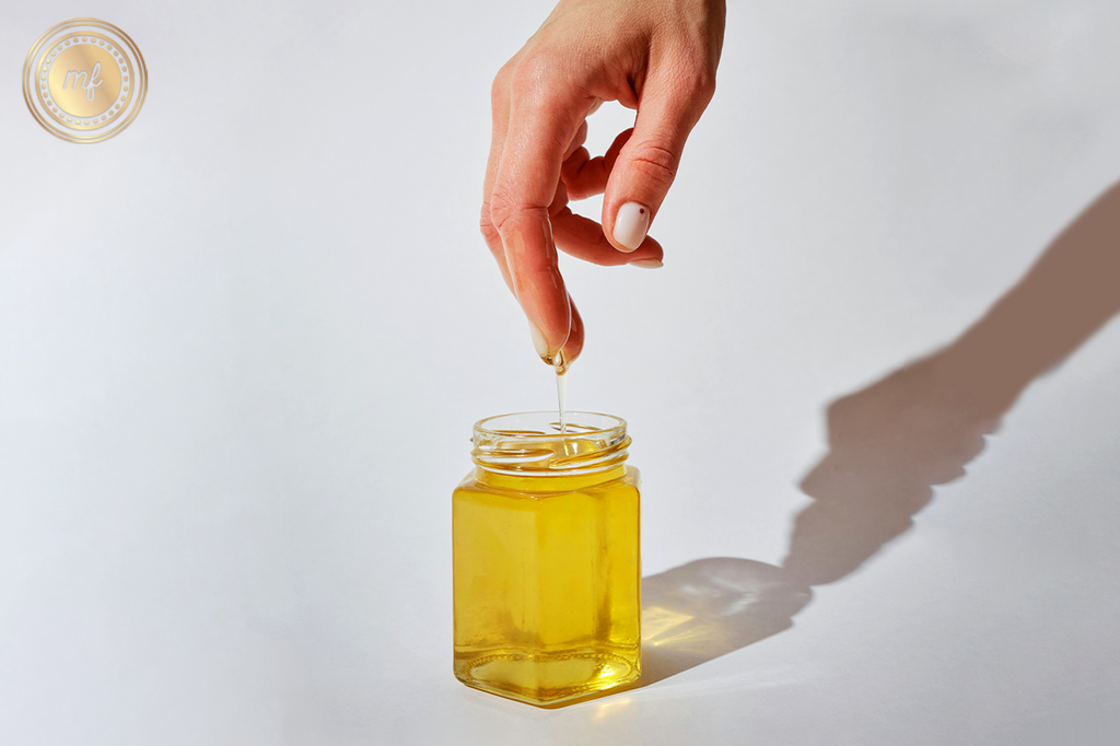 Person dipping their fingers into a jar with a yellow liquid.