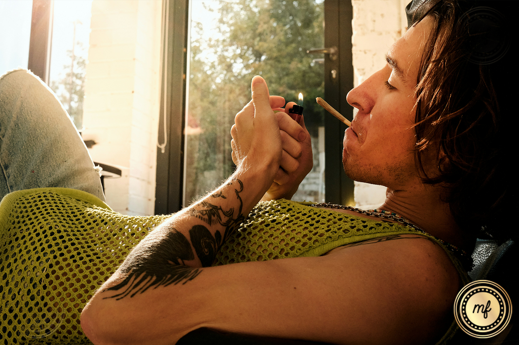 A man reclines on a sofa, cigarette in mouth, preparing to light it with a lighter