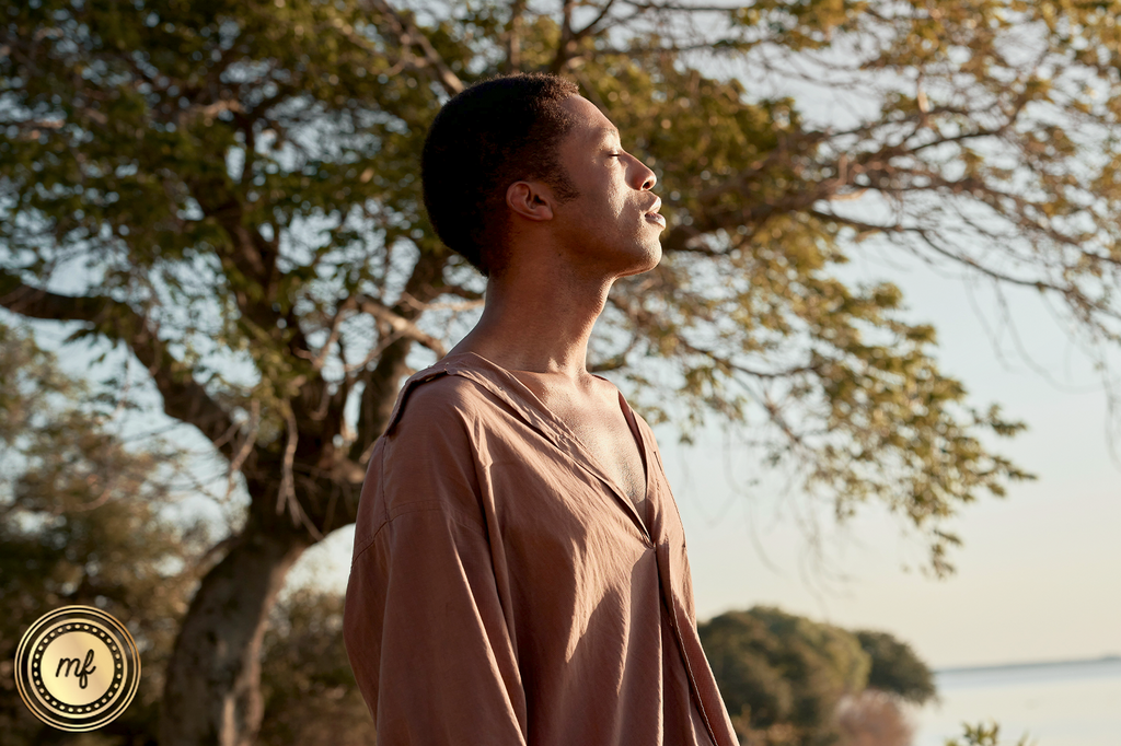 A man enjoying nature by the riverside, surrounded by trees, eyes closed, feeling the freshness