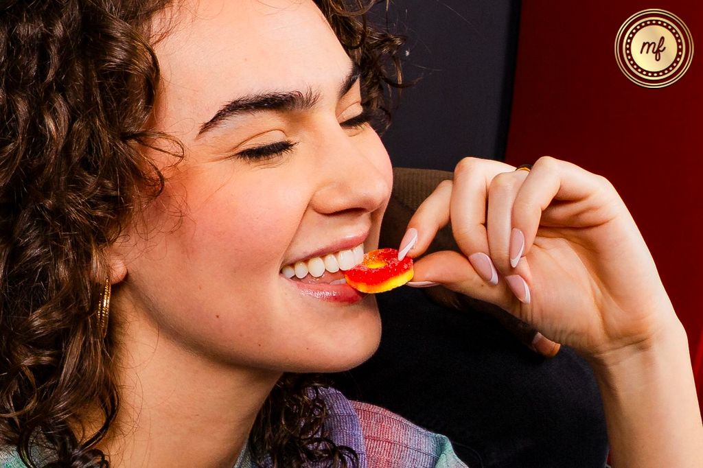 Woman taking a bite of a gummy worm, smiling.