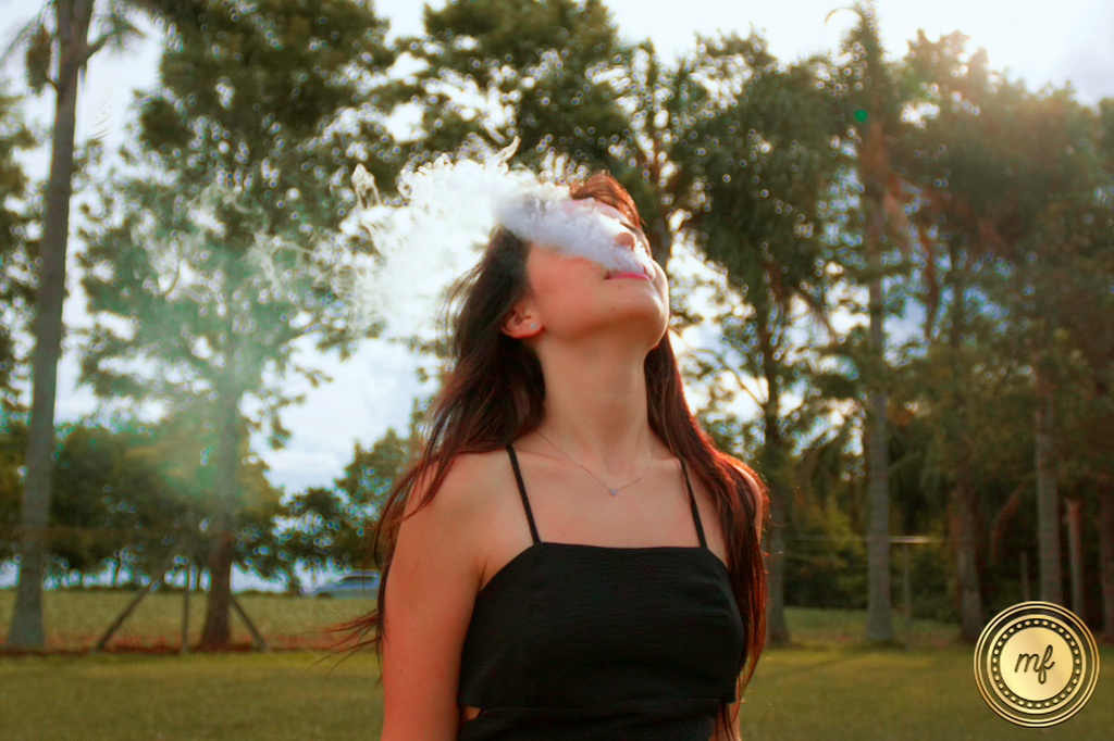 A woman standing outdoors exhales smoke, visibly enjoying the moment