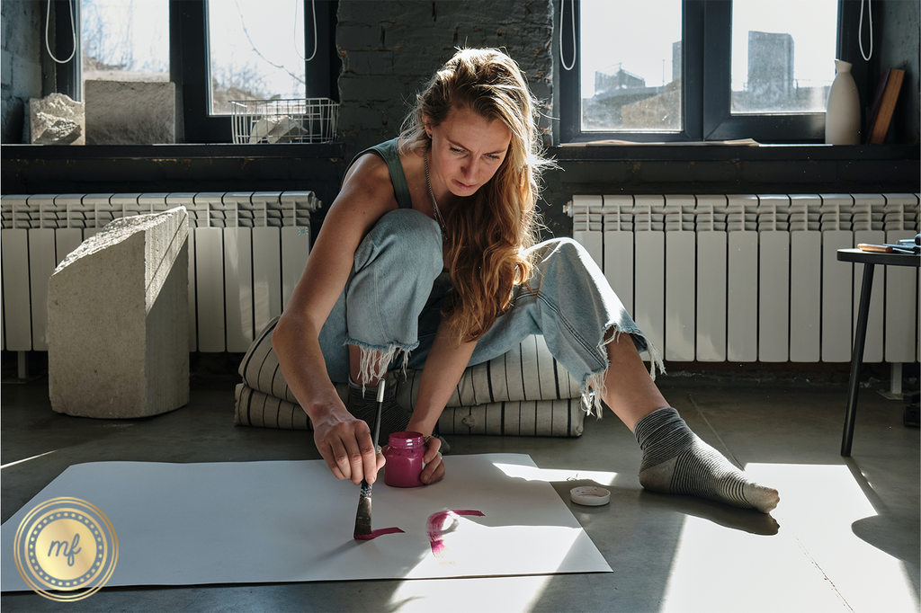 Woman in an apartment painting on a white paper on the floor.