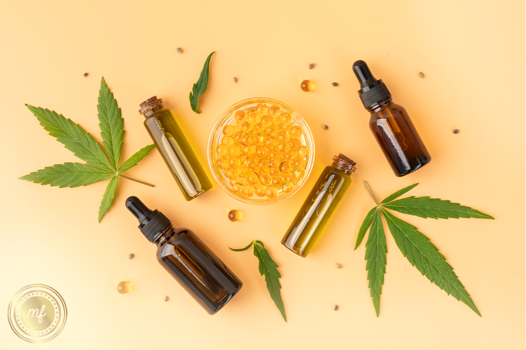 Cannabis tinctures next to cannabis capsules and cannabis leaves on a yellow surface.