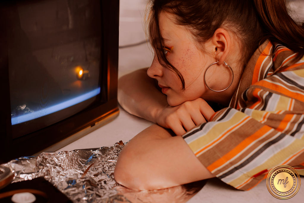Woman leaning on a table with her face very close to a TV with a black screen.