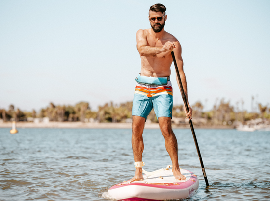 man balancing on a stand up paddle board, paddling forward