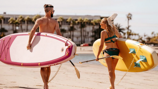 Man and woman carrying paddle boards on the beach