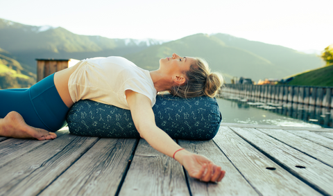 Frau liegt in der Yin Yoga Haltung Saddler auf einem Steg vor einem Bergpanorama