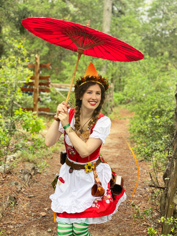 Dallas in a gnome outfit squatting underneath the parasol raised above her head