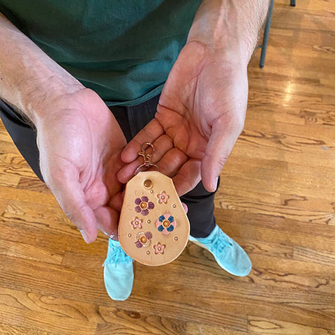 student showing luggage tag style keychain in the palm of their hand. Has small mandala type flower designs. 