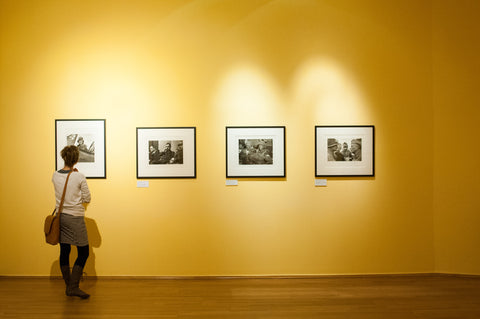 A woman looks at images of black and white photography in a gallery. The gallery walls are bright yellow.