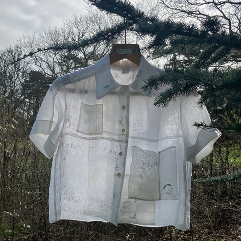 white shirt made from a patchwork of antique hankies, shown hanging from a tree branch with the light behind it