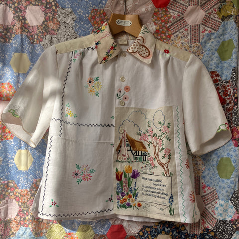 Recycled linen shirt with embroidered thatched cottage panel. Pictured against a vintage patchwork quilt