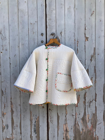 A cream coloured quilt jacket with green buttons and colourful binding hanging on a  grey garage door