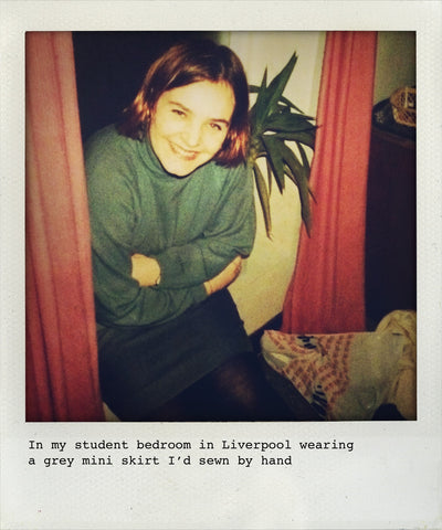 a 1990s student sits by a window wearing a blue roll neck and short grey skirt