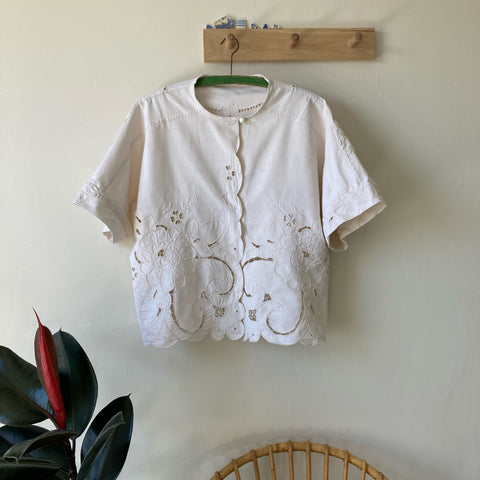 White cotton top made from a vintage tablecloth, hanging on a wooden hook