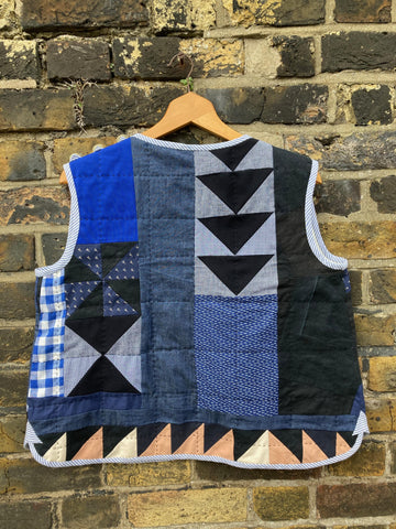 Hand quilted patchwork gilet/vest/body warmer/waistcoat in shades of blue, back view, on a hanger against a brick wall