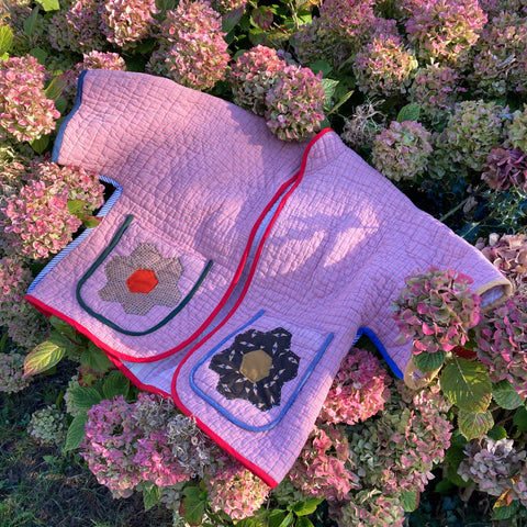 pink quilted jacket with patchwork pockets and red binding on a pink hydrangea bush