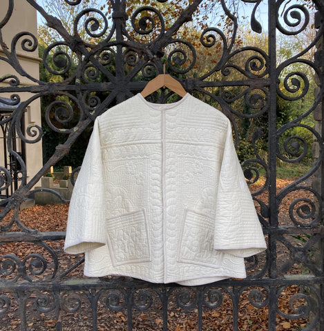 Cream-coloured quilted jacket with square patch pockets hanging on some swirly black iron gates