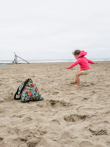 child jumping on a beach with a bag in view