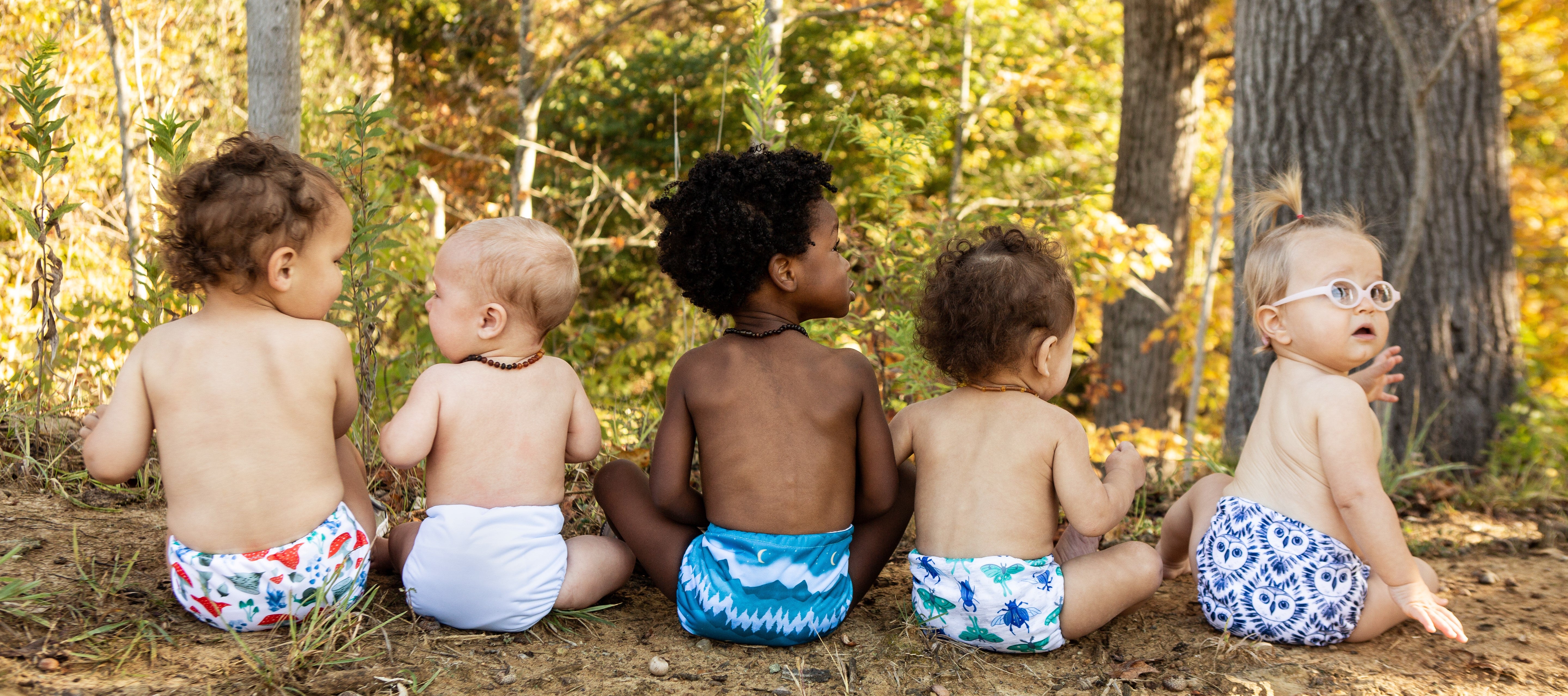 Image of five babies in a forest setting wearing Thirsties diapers in prints: Forest Frolic, Ice Blue, Mountain Twilight, Arthropoda, and Night Owl.