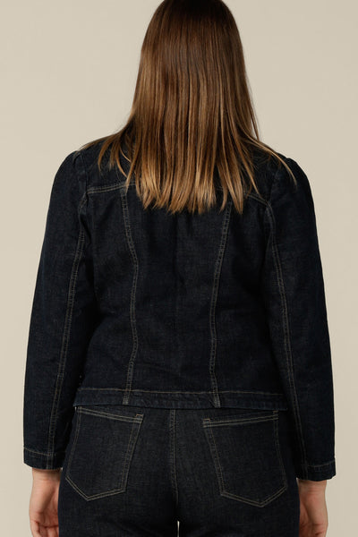 Back view of a size 12 woman wearing a denim blazer-style jacket by Australian and New Zealand women's clothing label, L&F. Worn with high-waisted, flared cut jeans in comfort stretch, conscious denim, this denim jacket is tailored to fit sizes 8 to 24.