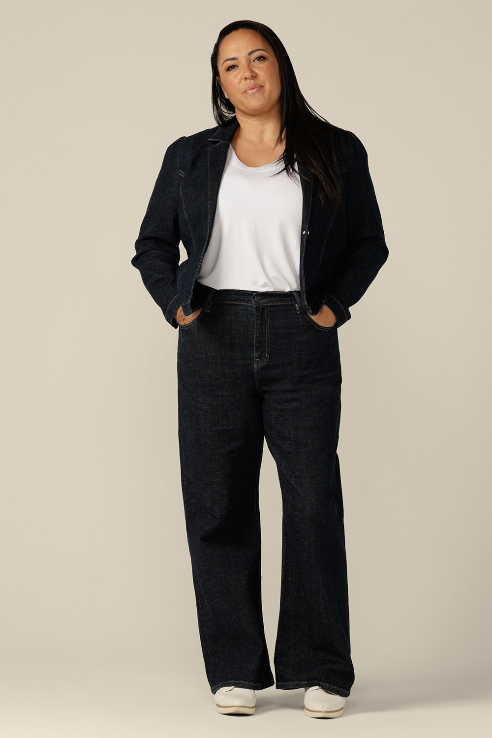 A size 18 woman wears a blazer-style jacket in midnight denim by Australian and New Zealand women's clothing label, L&F. Worn with high-waisted, flared cut jeans in comfort stretch, ethicalcdenim, this denim jacket is made to fit sizes 8 to 24.