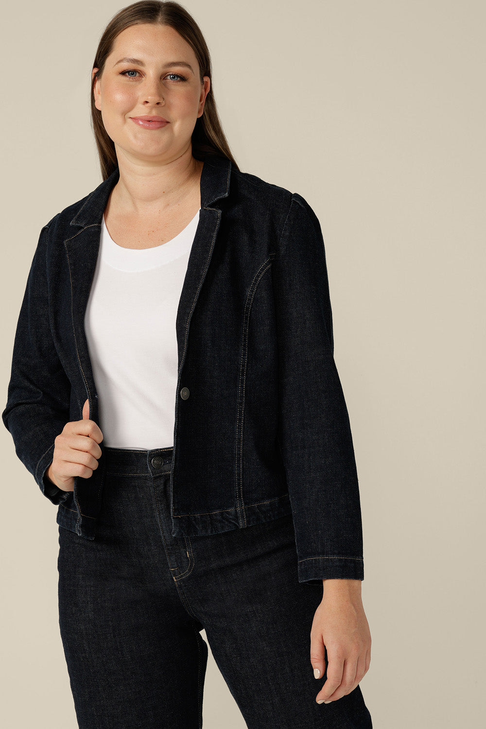 A size 12 woman wears a denim blazer-style jacket by Australian and New Zealand women's clothing label, L&F. Worn with high-waisted, flared cut jeans in comfort stretch, sustainable denim, this denim jacket is tailored to fit sizes 8 to 24.