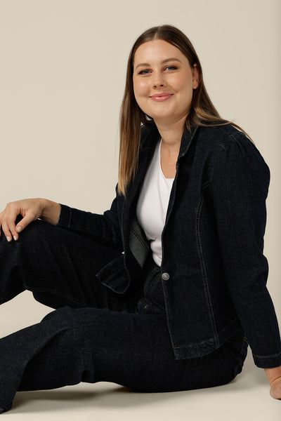 A size 12 woman wears a blazer-style, midnight denim jacket by Australian and New Zealand women's clothing label, L&F. Worn with high-waisted, flared cut jeans in comfort stretch, ethical denim, this denim jacket is tailored to fit sizes 8 to 24. Shop now for jeans with free shipping to New Zealand