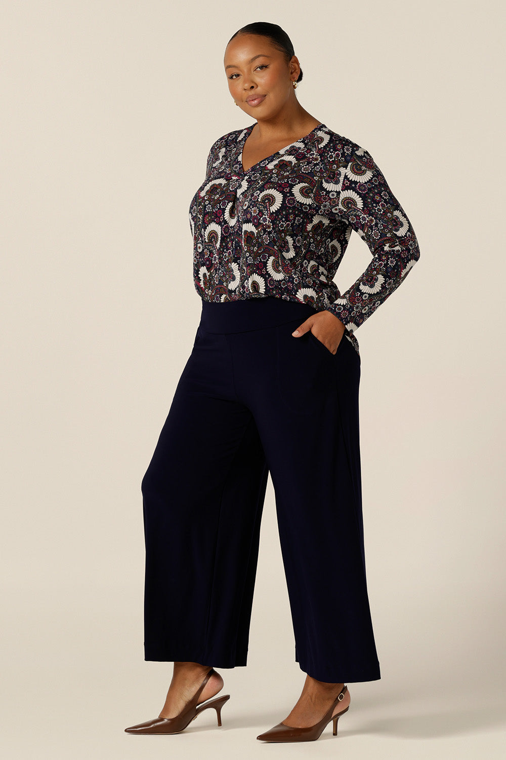 A size 18, plus size woman wears a long-sleeve, V-neck top in paisley print jersey. Worn with wide leg navy pants, this work top s comfortable for corporate and weekend wear.  Made in Australia by Australian and New Zealand women's clothing label, L&F.
