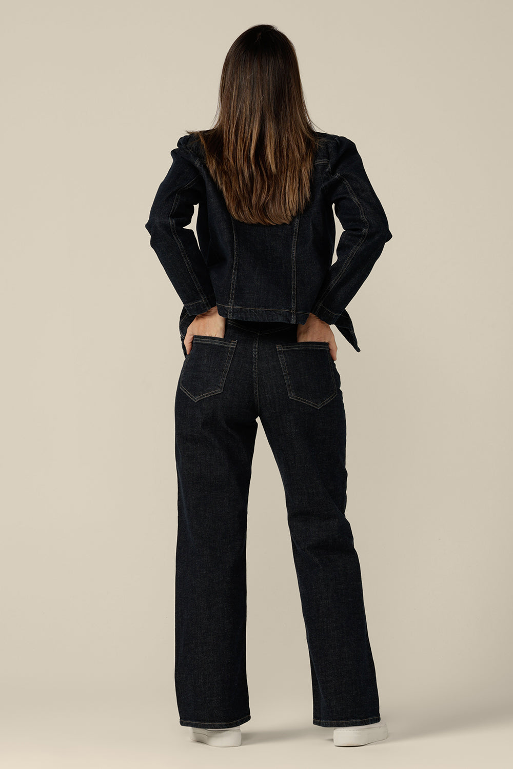Back view of a size 8 woman wearing a blazer-style jacket in midnight denim by Australian and New Zealand women's clothing label, L&F. Worn with high-waisted, flared cut jeans in comfort stretch, sustainable denim, this denim jacket is tailored to fit sizes 8 to 24.