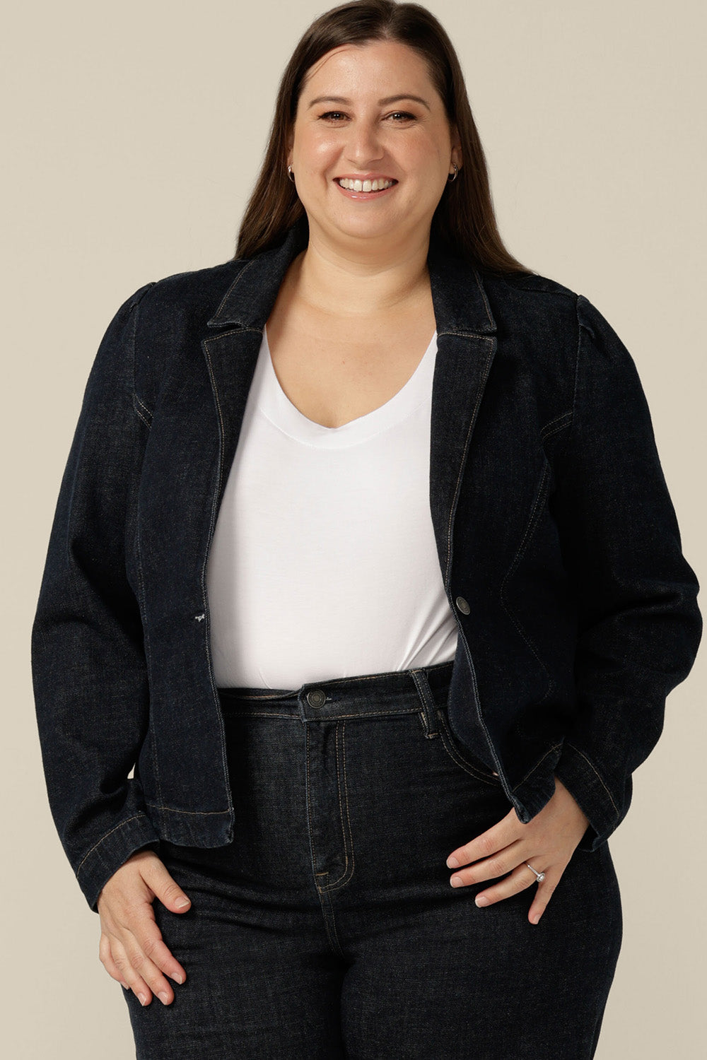 A size 16 woman wears a blazer-style jacket in midnight denim by Australian and New Zealand women's clothing label, L&F. Worn with high-waisted, flared cut jeans in comfort stretch, organic cotton denim, this denim jacket is tailored to fit sizes 8 to 24.