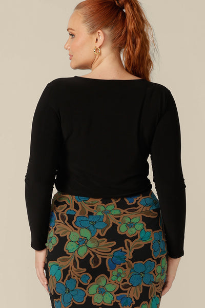 Back view of a women's, long sleeve, boat neck top in black jersey worn with floral print tube skirt. Australian-made, this is a good work top. Shop women's tops in an inclusive 8-24 size range now.
