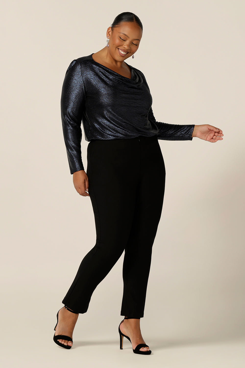 A long sleeve occasionwear top with cowl neck in shimmering midnight blue jersey fabric, size 18 is worn with slim leg, black evening trousers, size 18. Both plus size occasionwear garments are made in Australia in sizes 8 to 24 by Australian and New Zealand women's fashion label, L&F.