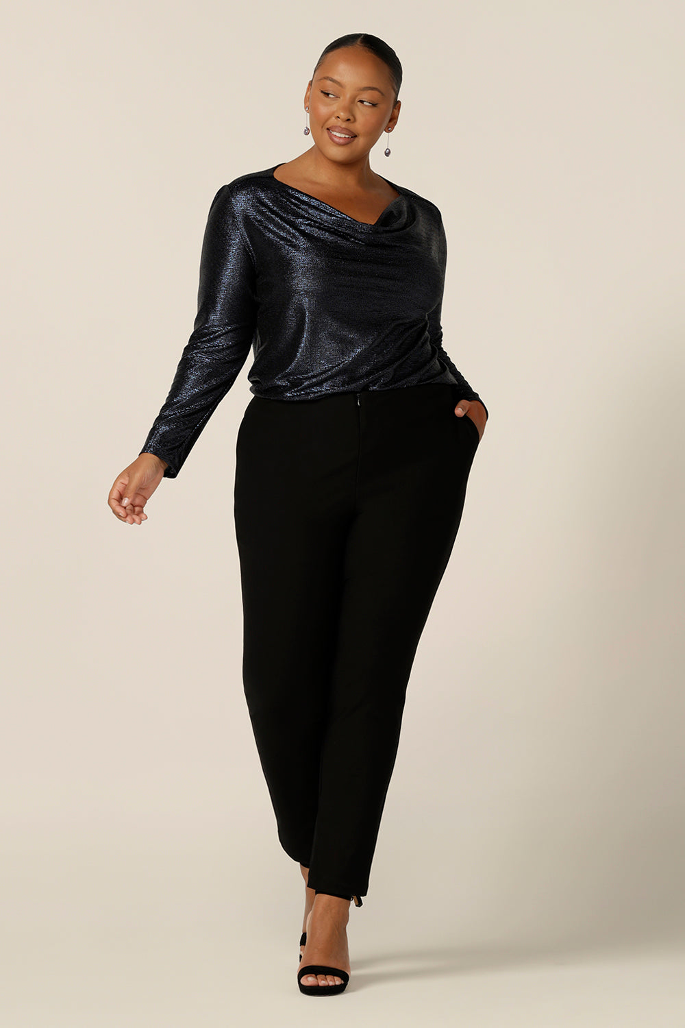 A long sleeve occasionwear top with cowl neck in shimmering midnight blue jersey fabric, size 18 is worn with slim leg, black evening pants, size 18. Both plus size occasionwear garments are made in Australia in sizes 8 to 24 by Australian and New Zealand women's clothing brand, L&F.