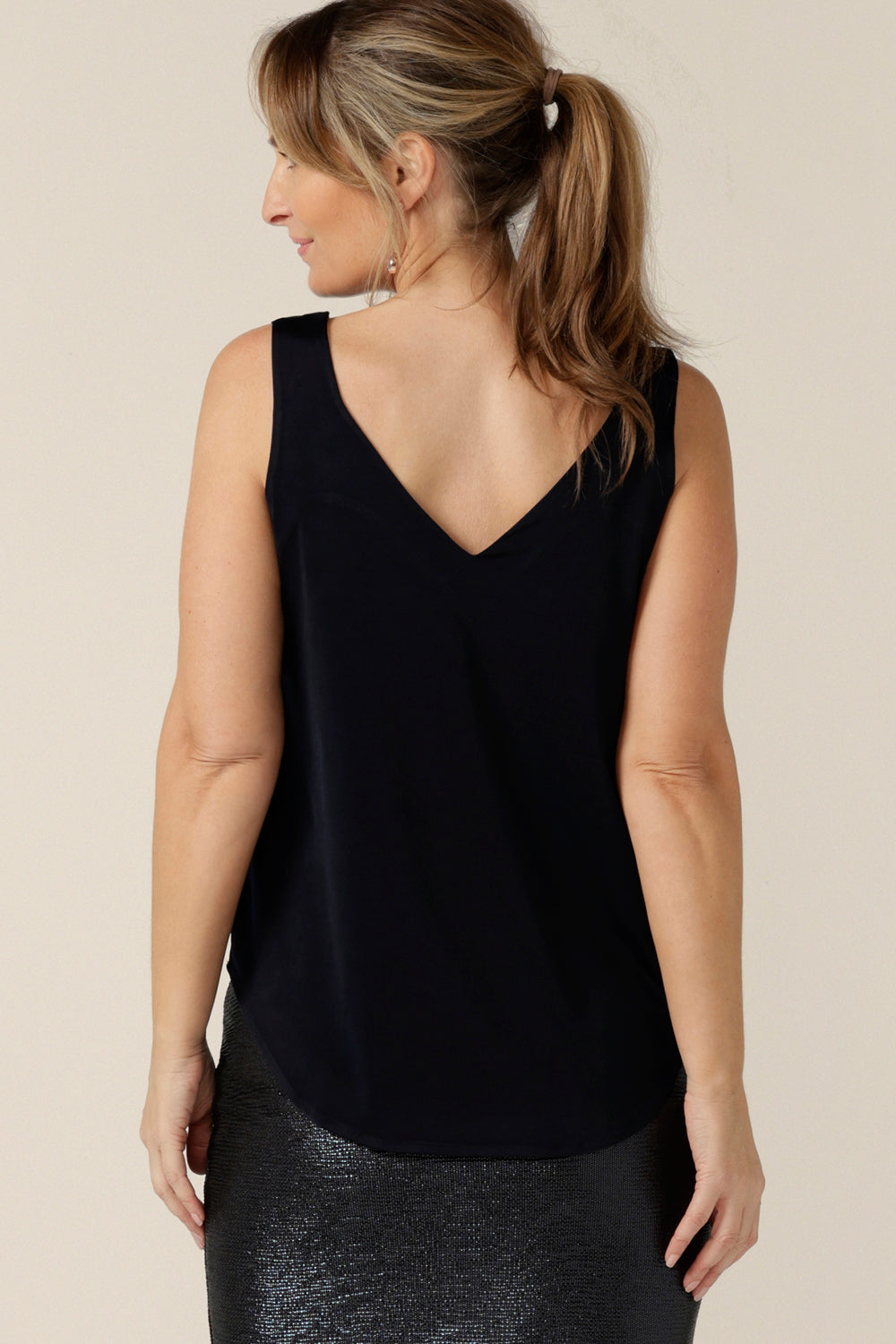 Back view of a woman wearing a V-neck, navy cami top with wide shoulder straps. Made in Australia by Australian and New Zealand women's clothing company, this slinky jersey top wears well with evening and occasionwear skirts, pants and suit jackets.