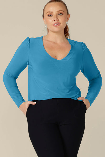 A curvy, size 12 woman wears a long sleeve, V-neck top in Opal blue jersey. Made in Australia by Australian and New Zealand women's clothing company, L&F, this top is available for shipping across Australia and New Zealand in sizes 8 to 24.
