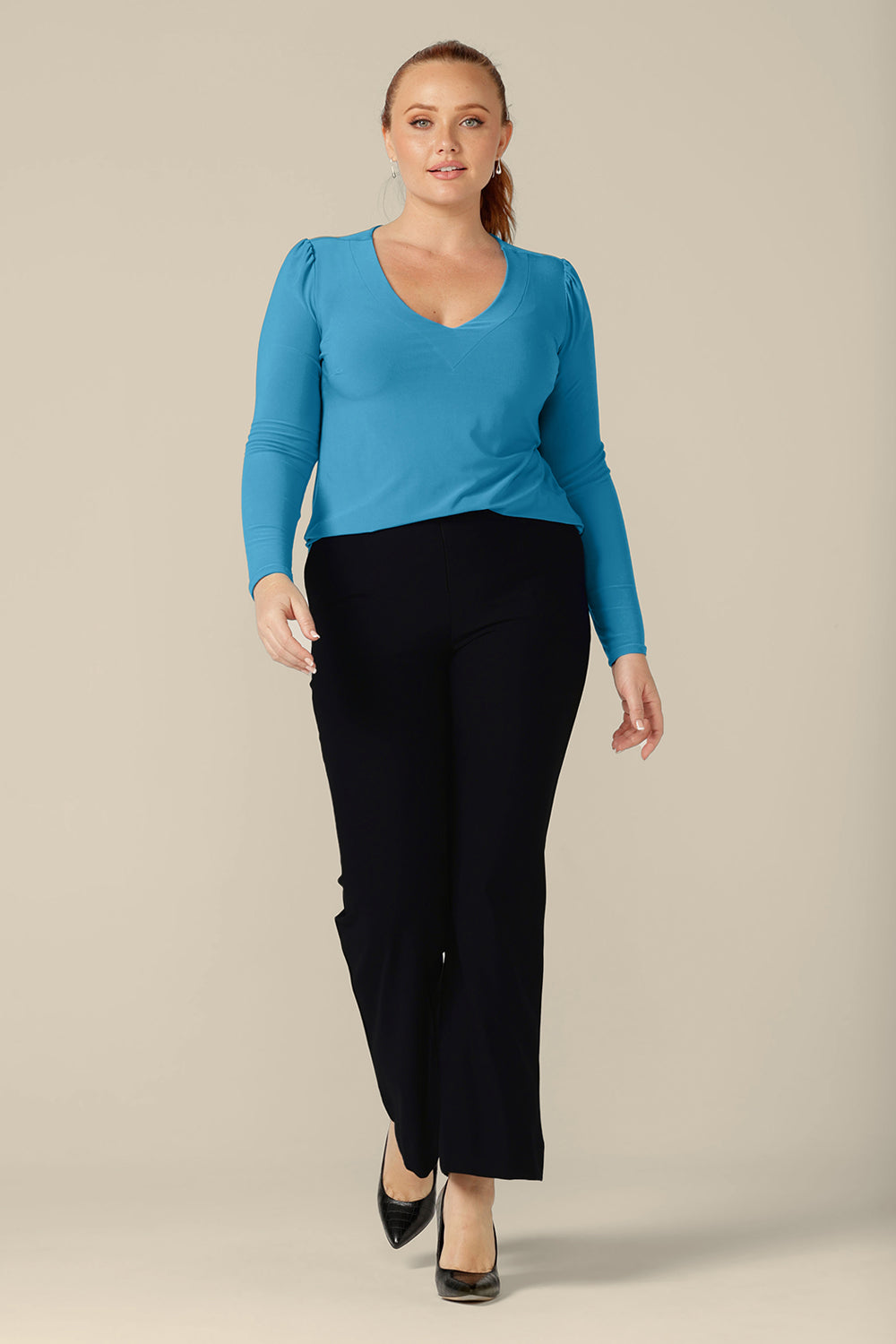 A vsize 12, curvy woman wears a long sleeve, V-neck top in Opal blue jersey with straight-leg navy work pants. Made in Australia by Australian and New Zealand women's clothing company, L&F, shop tops in inclusive sizes, 8 to 24 with free shipping to New Zealand.