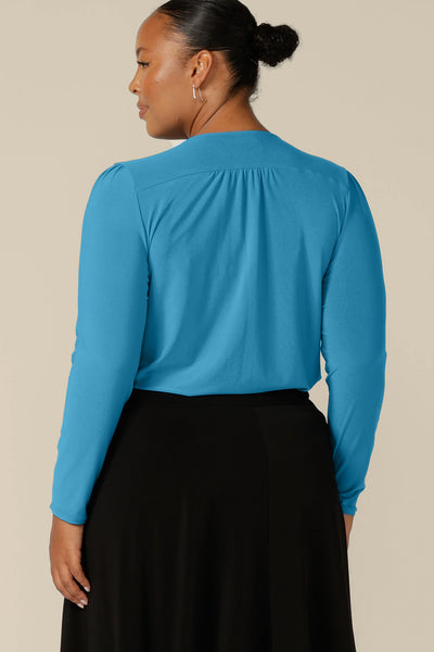 Back view of a fuller figure, size 18 woman wearing a long sleeve, V-neck top in Opal blue jersey. Made in Australia by Australian and New Zealand women's clothing company, L&F, this work top is available for shipping in sizes 8 to 24.