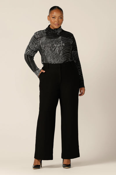 A fuller figure woman wears a long sleeve, woolly knit turtleneck top, size 18, in an abstract black and white pattern. A warm winter top, this women's polo neck top is worn with a high-waisted, wide leg, black pants.