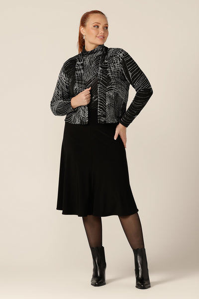 A blend of jacket and cardigan, this textured knit 'jacardi' is a good way to layer up for winter. Worn by a curvy, size 12 woman, this knit jacket is worn with a flared, black skirt and matching polo neck top to create a modern twinset with a winter cardigan. 