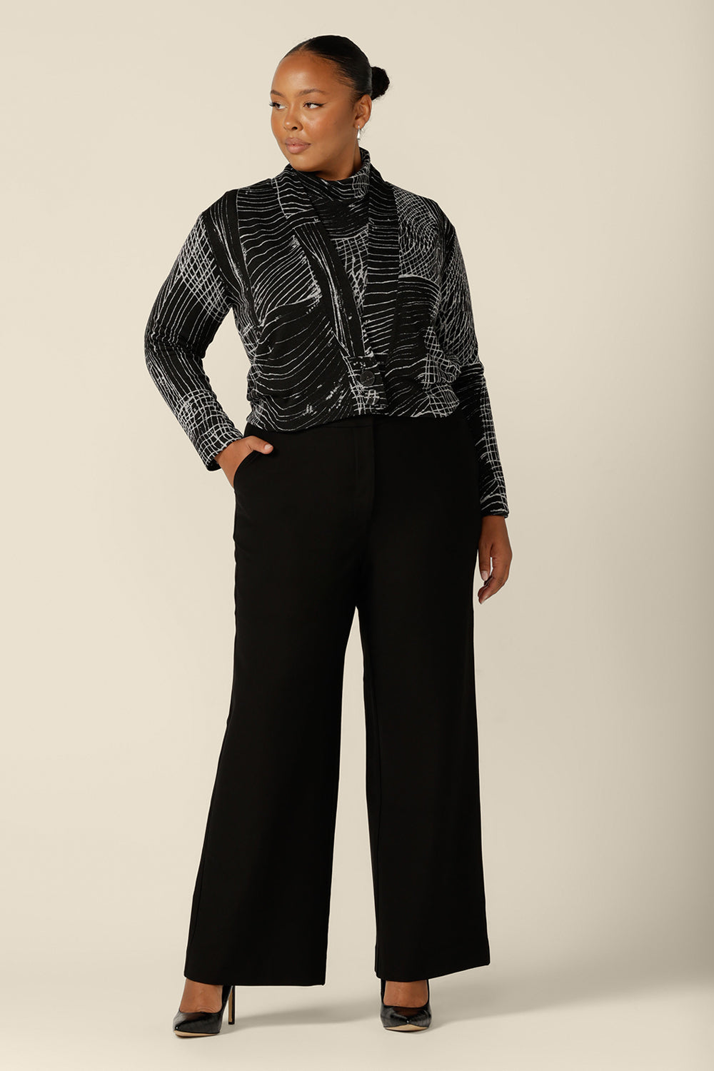 A blend of jacket and cardigan, this textured knit 'jacardi' is a good way to layer up for winter. Worn by a plus size, size 18 woman, this knit jacket is worn with tailored black trousers and a matching polo neck top to create a modern twinset for work wear and weekend wear.  