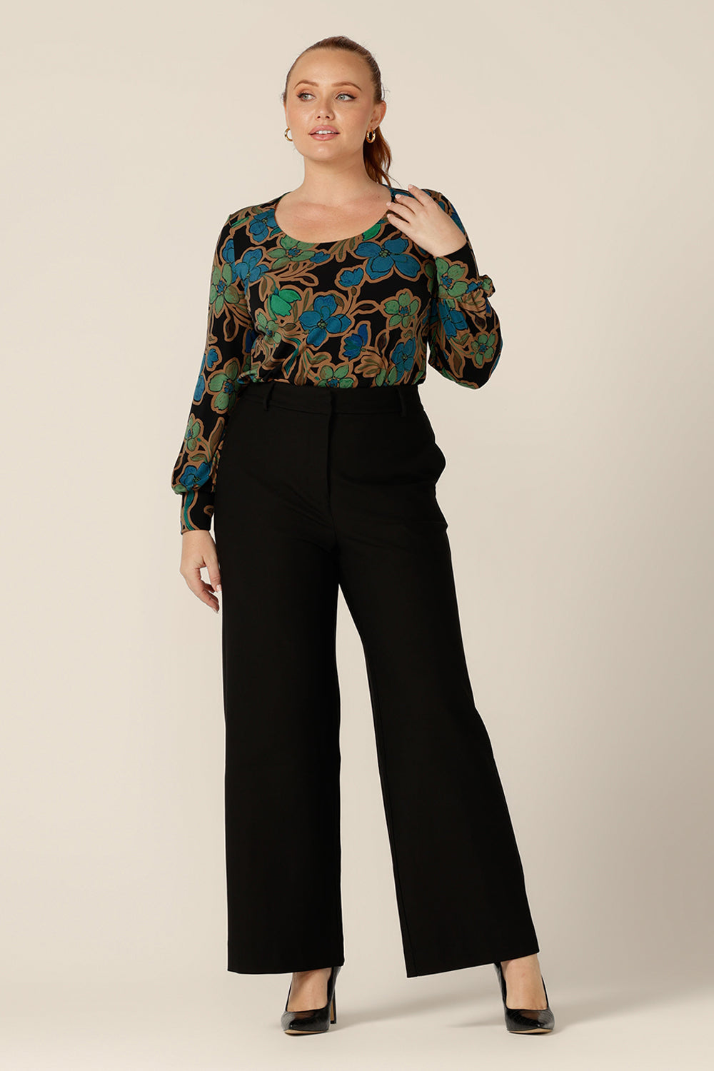 A size 12 woman wears a long sleeve top with scoop neck with tailored, wide leg, black pants. Both made in Australia by Australian and New Zealand women's clothing brand, L&F both pants and top are available to shop in sizes 8 to 24.