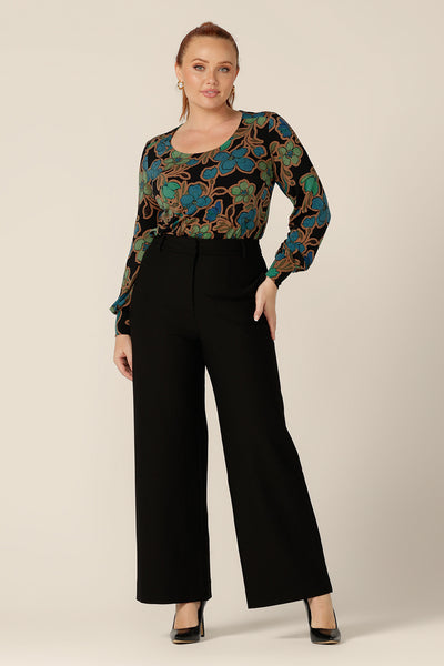 A size 12 woman wears a long sleeve top with scoop neck, with tailored, wide leg, black trousers. Both made in Australia by Australian and New Zealand women's clothing brand, L&F both work pants and the jersey top are available to shop in sizes 8 to 24.