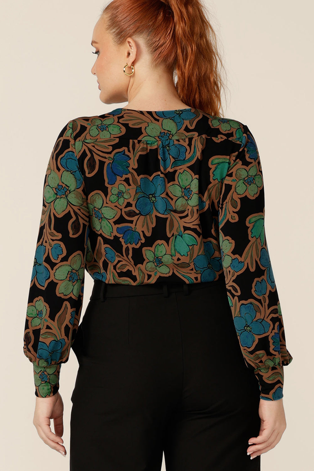 Back view of a size 12 woman wearing a long sleeve top with scoop neck. Feminine tailoring blouses full-length cuffed sleeves at the wrists to shape this floral print jersey top. Shop Australian-made tops in sizes 8 to 24.