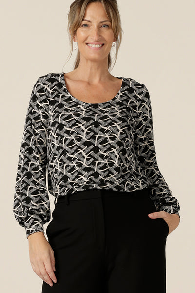 A size 10 woman wears a long sleeve top with bishop sleeve cuffs and a scoop neck in black and white print jersey.  Made in Australia by Australian and New Zealand women's clothing brand, L&F this women's work top is available to shop in sizes 8 to 24.