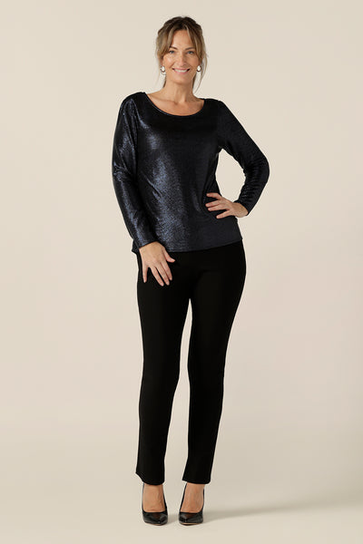 A size 10, 40-plus woman wears a shimmering midnight blue sparkly top with high scoop neck and long sleeves. Worn with slim leg, black evening pants, this is a simple and easy-to-wear, comfortable eveningwear top. Made in Australia in sizes 8 to 24.