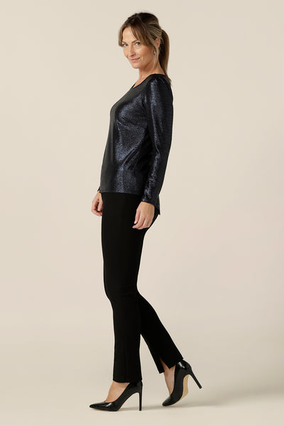 side view of a size 10, 40-plus woman wears a shimmering midnight blue sparkly top with high scoop neck and long sleeves. Worn with slim leg, black evening pants, this is a simple and easy-to-wear, comfortable eveningwear top. Made in Australia in sizes 8 to 24.